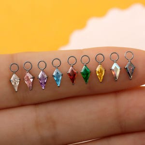 May include: A row of nine small kite-shaped charms, each featuring a faceted gemstone in a different color including clear, pink, purple, blue, red, green, yellow, iridescent, and dark gray, all set in dark metal with a circular jump ring.
