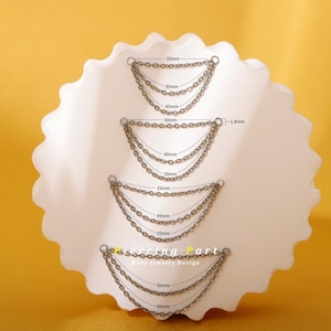 May include: Close-up of four sets of silver-colored body jewelry chains, each with multiple strands. Measurements in millimeters are labeled on each chain set. The jewelry is displayed on a white, scalloped surface against a yellow background. Text reads "Piercing Part Body jewelry Design."