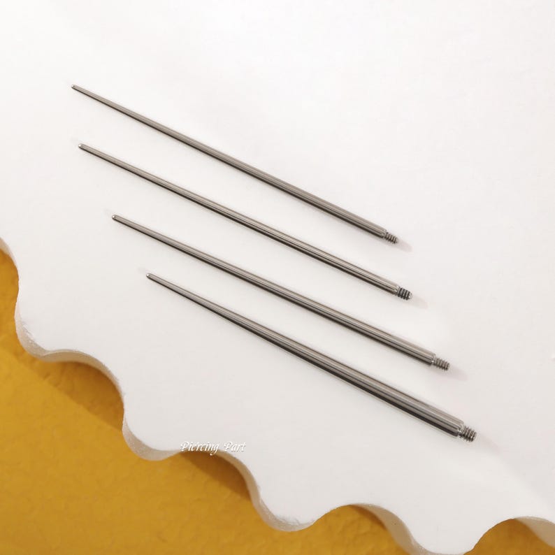 May include: Four silver piercing needles of different lengths, laid out on a white surface.