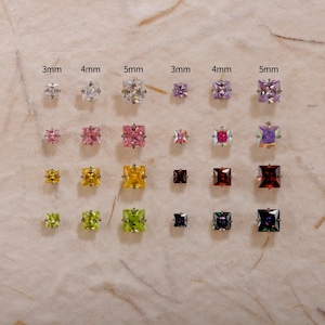 May include: A collection of square-cut stud earrings in various colors, including clear, pink, yellow, and green. Each earring is set in a silver-tone metal and is labeled with its size in millimeters, ranging from 3mm to 5mm.
