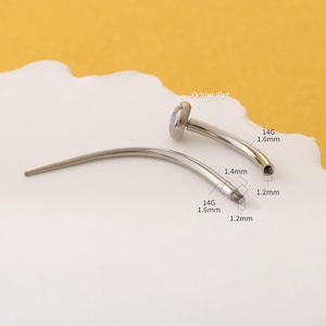 May include: A silver curved barbell with a clear opal gemstone on one end. The barbell is 1.6 mm thick and 1.4 mm wide. The barbell is 1.2 mm thick at the threaded end.