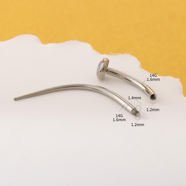 May include: A silver curved barbell with a clear opal gemstone on one end. The barbell is 1.6 mm thick and 1.4 mm wide. The barbell is 1.2 mm thick at the threaded end.