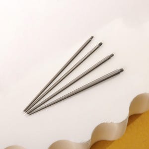 May include: Four silver metal piercing needles, arranged in a fan shape, on a white surface.