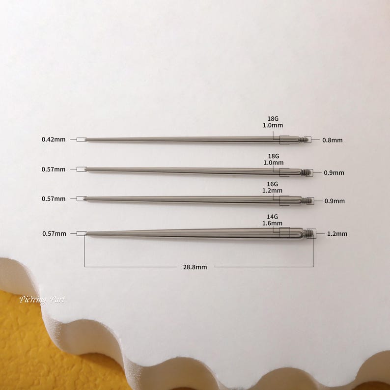 May include: Four stainless steel piercing needles of different gauges and lengths. The needles are laid out horizontally on a white surface. The gauges and lengths are labeled in millimeters. The needles are 0.42mm, 0.57mm, 0.57mm, and 0.57mm in length. The gauges are 18G, 18G, 16G, and 14G. The needles are 1.0mm, 1.0mm, 1.2mm, and 1.6mm in diameter.