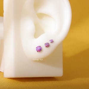 May include: Three purple opal earrings with a prong setting. The earrings are different sizes and are shown on a white ear model.