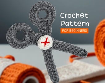 May include: Crochet pattern for beginners. A gray crocheted pair of scissors with a white button and a red cross.