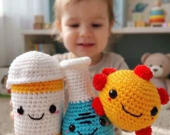 May include: Three crocheted plush toys featuring a white and yellow pill bottle, a blue and white laboratory flask, and a round yellow sun-like character with red accents. Each toy has black safety eyes and a stitched smiling mouth.