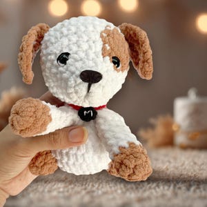 May include: A white and brown crocheted dog toy with a red collar and a black letter "M" on the collar.