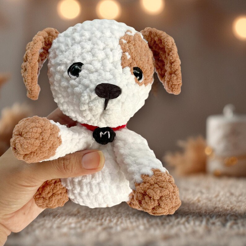 May include: A white and brown crocheted dog toy with a red collar and a black letter "M" on the collar.