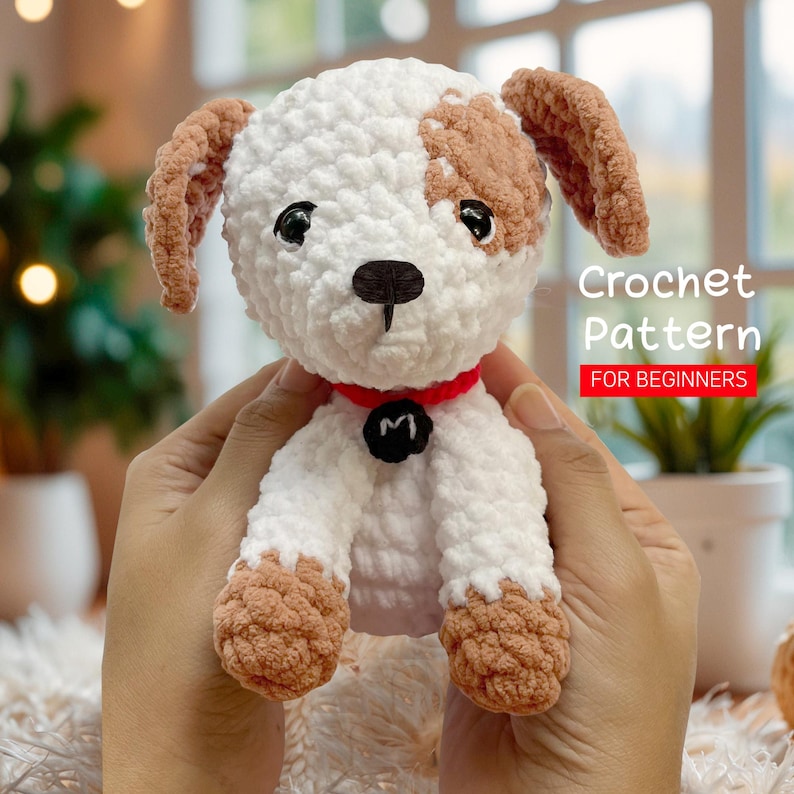 May include: Crochet pattern for beginners. A white and brown crocheted puppy with a red collar and a black letter M on the collar.