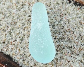 Könnte beinhalten: Ein hellblaues Stück Seetangglas mit einer glatten, abgerundeten Form. Das Glas ist durchscheinend und hat eine leicht gefrostete Oberfläche.