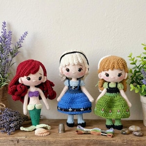 Peut inclure: Trois poup&eacute;es au crochet faites &agrave; la main : une sir&egrave;ne aux cheveux roux, une poup&eacute;e en robe bleue et une poup&eacute;e en robe verte. Les poup&eacute;es sont expos&eacute;es sur une &eacute;tag&egrave;re en bois avec de la lavande, un d&eacute; &agrave; coudre et du fil &agrave; broder.