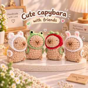 May include: Four small, tan, crocheted capybara plush toys arranged in a row. Each capybara wears a different crocheted hood: one white with ears, one green frog hood, one red strawberry hood, and one white with rabbit ears. Text reads: Cute capybara with friends.