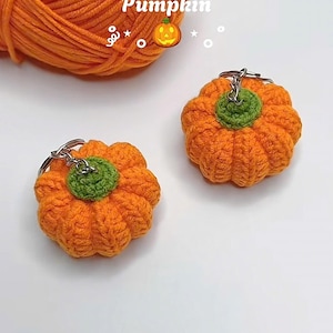 Puede incluir: Dos llaveros de calabaza naranja de ganchillo con tallos verdes. Los llaveros est&aacute;n junto a una madeja de hilo naranja. La palabra "Pumpkin" est&aacute; escrita encima de las calabazas.