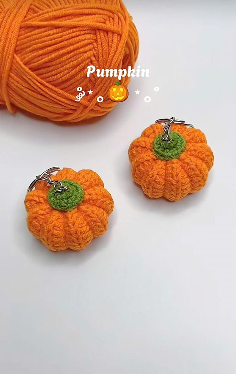 Puede incluir: Dos llaveros de calabaza naranja de ganchillo con tallos verdes. Los llaveros est&aacute;n junto a una madeja de hilo naranja. La palabra "Pumpkin" est&aacute; escrita encima de las calabazas.