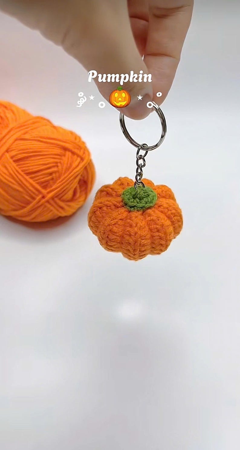 Puede incluir: Un llavero de calabaza naranja hecho a mano con ganchillo y un tallo verde. La palabra "Pumpkin" est&aacute; escrita encima del llavero. Una madeja de hilo naranja est&aacute; en el fondo. El llavero est&aacute; unido a un llavero plateado.
