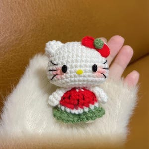 Peut inclure: Poup&eacute;e au crochet faite &agrave; la main, ressemblant &agrave; un personnage de dessin anim&eacute; populaire. La poup&eacute;e blanche a des yeux noirs, des moustaches et un n&oelig;ud rouge. Elle porte une robe sur le th&egrave;me de la past&egrave;que, rouge et verte. La poup&eacute;e est tenue dans une main.