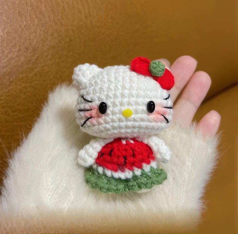 Peut inclure: Poup&eacute;e au crochet faite &agrave; la main, ressemblant &agrave; un personnage de dessin anim&eacute; populaire. La poup&eacute;e blanche a des yeux noirs, des moustaches et un n&oelig;ud rouge. Elle porte une robe sur le th&egrave;me de la past&egrave;que, rouge et verte. La poup&eacute;e est tenue dans une main.