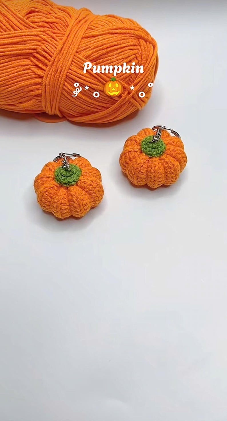 Puede incluir: Dos llaveros de calabaza naranja de ganchillo con tallos verdes sobre una superficie blanca. Una madeja de hilo naranja y la palabra "Pumpkin" est&aacute;n en el fondo. Los llaveros est&aacute;n hechos a mano.