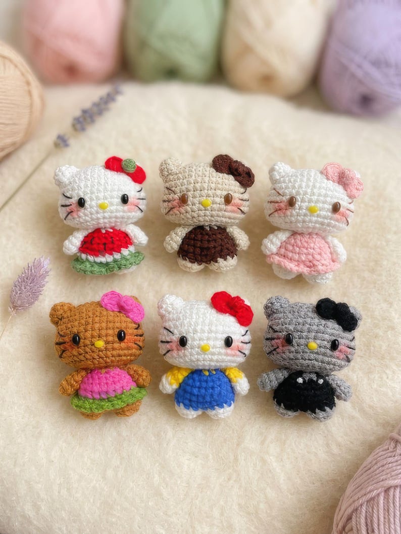 Peut inclure: Six poup&eacute;es au crochet faites &agrave; la main en forme de chat, chacune avec des tenues et des accessoires uniques. Les poup&eacute;es sont blanches, beiges, marron et grises, avec des robes et des n&oelig;uds color&eacute;s. Les poup&eacute;es sont dispos&eacute;es sur une surface cr&egrave;me.