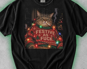 May include: A black short-sleeve t-shirt featuring a graphic of a tabby cat wearing a red and green patterned holiday sweater with the text FESTIVE AS FUCK. The cat is depicted with a cigarette and wrapped in colorful Christmas lights.