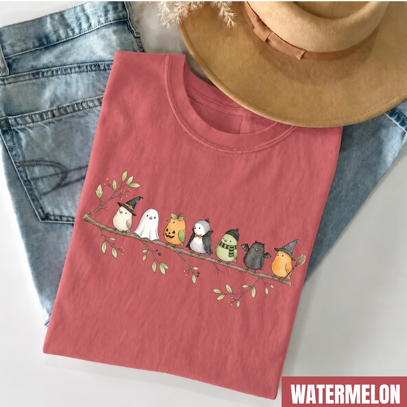 Peut inclure: Un t-shirt couleur past&egrave;que orn&eacute; d'un motif repr&eacute;sentant sept petits oiseaux perch&eacute;s sur une branche. Les oiseaux portent divers costumes, dont une sorci&egrave;re, un fant&ocirc;me, une citrouille, un vampire, un oiseau avec une &eacute;charpe, une chauve-souris.