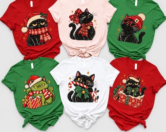 May include: A collection of six short-sleeve t-shirts in red, light pink, green, and white, each featuring a graphic illustration of a black cat with holiday-themed accessories like Santa hats, scarves, plaid bows, and gift boxes.