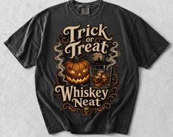 May include: A charcoal gray t-shirt featuring a graphic print with the text Trick or Treat and Whiskey Neat. The design includes a carved jack-o'-lantern, a glass of whiskey with ice, swirling smoke, a silhouette of a house, and a small skull.
