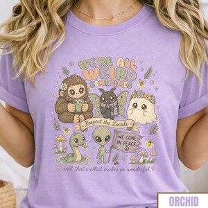 May include: Orchid purple t-shirt with the text "WE'RE ALL WEIRD SOMETIMES" and a graphic of whimsical creatures. The graphic includes a Bigfoot, a moth, a ghost, a snake, and an alien. The phrase "Respect the Locals" is on a banner.