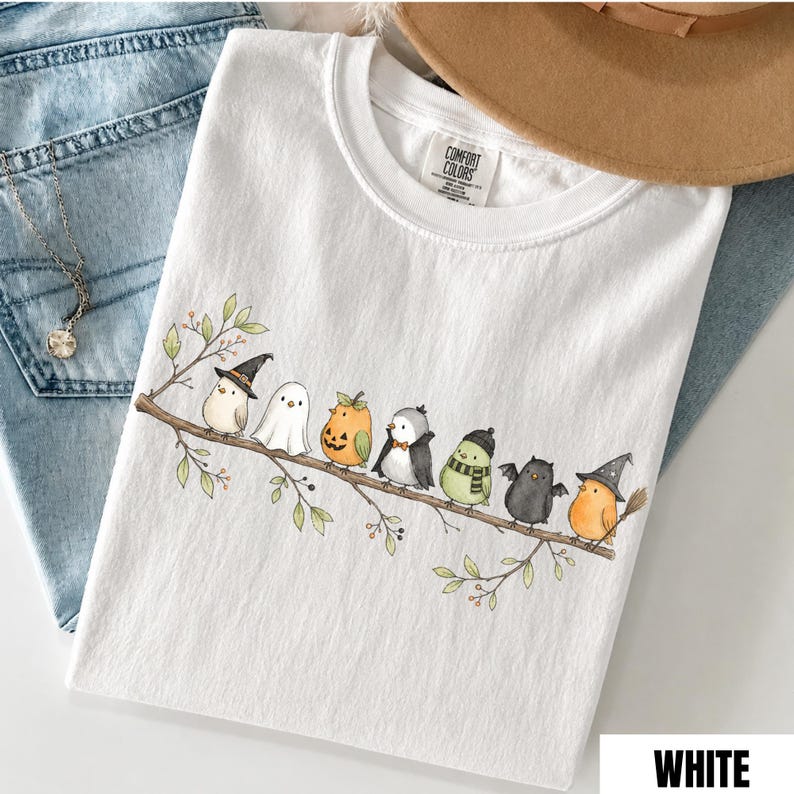 Peut inclure: Un t-shirt blanc orn&eacute; d'un motif repr&eacute;sentant huit petits oiseaux perch&eacute;s sur une branche. Les oiseaux portent divers costumes d'Halloween, notamment une sorci&egrave;re, un fant&ocirc;me, une citrouille, un vampire, un oiseau avec une &eacute;charpe, une chauve-souris et un magicien.