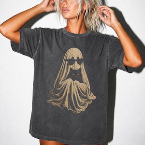 Peut inclure: Un t-shirt à manches courtes gris anthracite avec une impression graphique représentant un fantôme beige portant des lunettes de soleil noires et tenant un petit chat noir. Le t-shirt présente une texture délavée et un col rond.