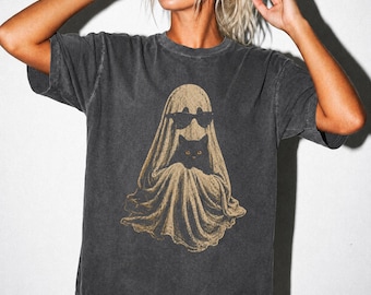 May include: A charcoal grey short-sleeve t-shirt featuring a graphic print of a beige ghost wearing black sunglasses and holding a small black cat. The shirt has a faded, washed-out texture and a crew neckline with a relaxed, boxy fit.