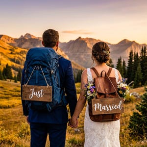 May include: Two rectangular wooden signs with white script text reading Just and Married, suspended by ropes from a blue hiking backpack and a brown leather backpack, respectively, with colorful wildflowers tucked into the leather bag straps.