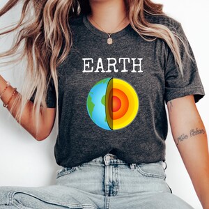 May include: Dark gray t-shirt with the word "EARTH" in white block letters above a colorful graphic of the Earth's cross-section. The graphic shows the planet's layers in blue, green, yellow, orange, and red.