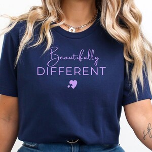 May include: Navy blue t-shirt with the words "Beautifully DIFFERENT" in a light purple script. A purple heart and star graphic is below the text. The shirt is a crew neck and made of a soft material.