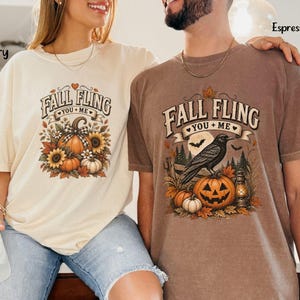 May include: Two short-sleeve t-shirts, one ivory and one espresso, each featuring a graphic print with the text "FALL FLING YOU + ME". The ivory shirt displays pumpkins and sunflowers, while the espresso shirt shows a crow, a jack-o'-lantern, and a lantern.