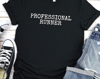 Puede incluir: Camiseta negra con el texto blanco "PROFESSIONAL RUNNER". La camiseta está doblada, con zapatillas deportivas blancas y negras y vaqueros azules visibles. La palabra "Black" está en la esquina superior izquierda.