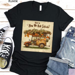 Może przedstawiać: Czarny t-shirt z kolorową grafiką zabytkowego pojazdu załadowanego produktami i napisem "This is How We Roll Sukkah?". Koszulka jest pokazana z czarnymi trampkami i niebieskimi dżinsami.