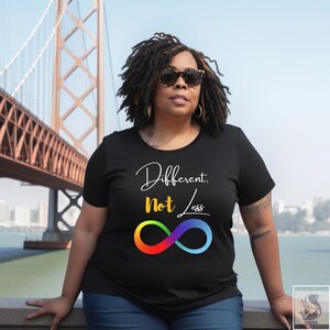 May include: Black t-shirt with the words "Different, Not Less" in white script and a rainbow infinity symbol. The shirt is worn by a person wearing sunglasses, with a bridge in the background.
