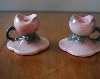 May include: Two pink and black ceramic candle holders shaped like a flower with a candle well in the center.