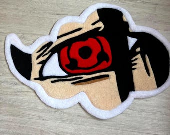 May include: A cloud-shaped rug featuring a stylized eye with a red iris and black pupil. The rug has a white border, beige skin tones, and black hair. The design is reminiscent of anime or manga art.