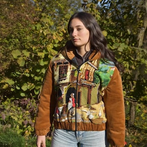 May include: A brown corduroy jacket with a colorful embroidered scene of a building and people. The jacket has a zipper closure and a hood.