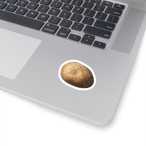 Può includere: Un adesivo di patata marrone con un contorno bianco. L'adesivo è su un laptop argentato.