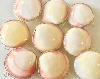 Könnte beinhalten: Neun runde, dekorative Boxen aus natürlichen Muscheln mit Messing-Scharnieren und Verschlüssen. Die Muscheln sind in einem zarten Rosa und Weiß mit einem Perlmutt-Glanz.