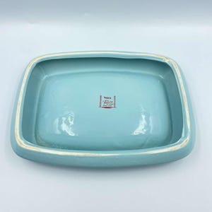 May include: A light blue ceramic dish with a white rim. The bottom of the dish has a red and white logo that reads "Ware  Rose  Made in Japan".