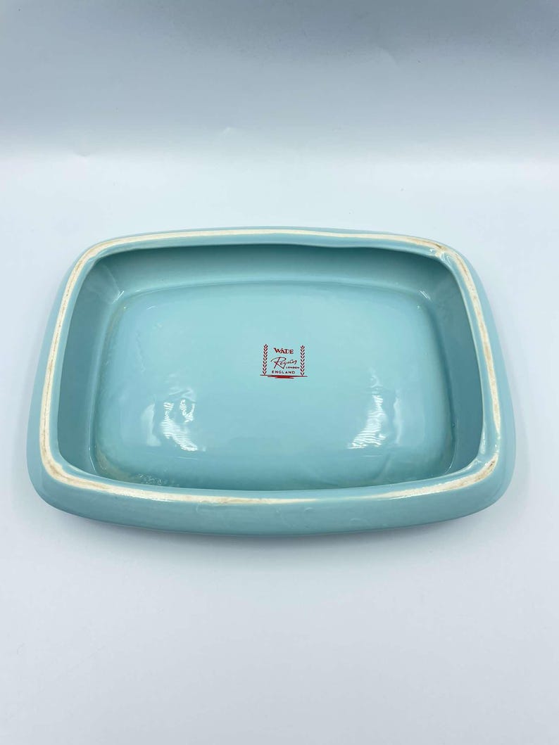 May include: A light blue ceramic dish with a white rim. The bottom of the dish has a red and white logo that reads "Ware  Rose  Made in Japan".