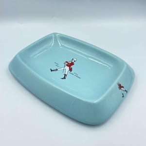 May include: A light blue ceramic ashtray featuring a walking man graphic and the text "Born 1820 - Still Going Strong".