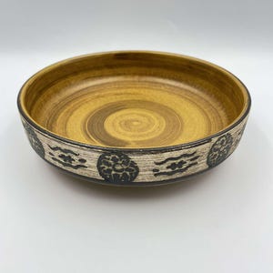Peut inclure: Un bol en céramique jaune avec un motif géométrique noir et blanc autour du bord. Le bol a un motif en spirale à l'intérieur.