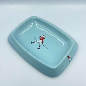 May include: A light blue ceramic ashtray featuring a red and white illustration of a man in riding attire. The text "BORN 1820 - STILL GOING STRONG" is printed on the ashtray.