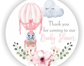 May include: A round sticker with a pink and white striped hot air balloon, a gray elephant, and a smiling cloud. The text reads "Thank you for coming to our Baby Shower" in pink script. Floral and leaf accents surround the bottom.